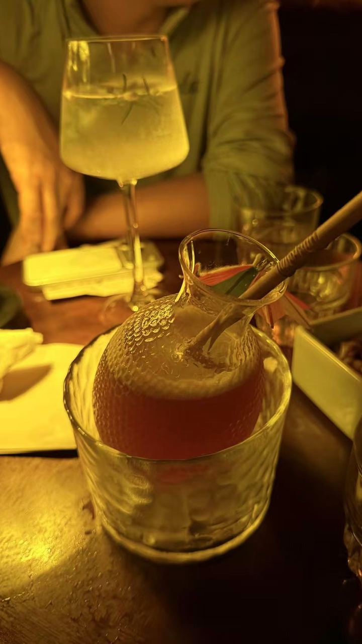 A cocktail served in a glass carafe on ice, in a dim, golden-lit bar.